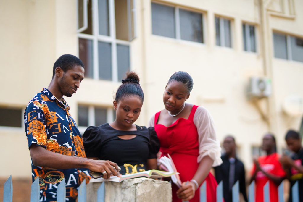 Three university students in Nigeria outdoors studying and discussing a book together.